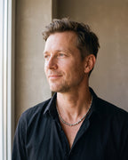 Man in a black fine cotton shirt by a window wearing the silver Atlas irregular bead chain