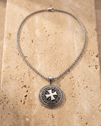The whole silver-tone Atlas Knights Templar cross medallion necklace lying on warm travertine stone