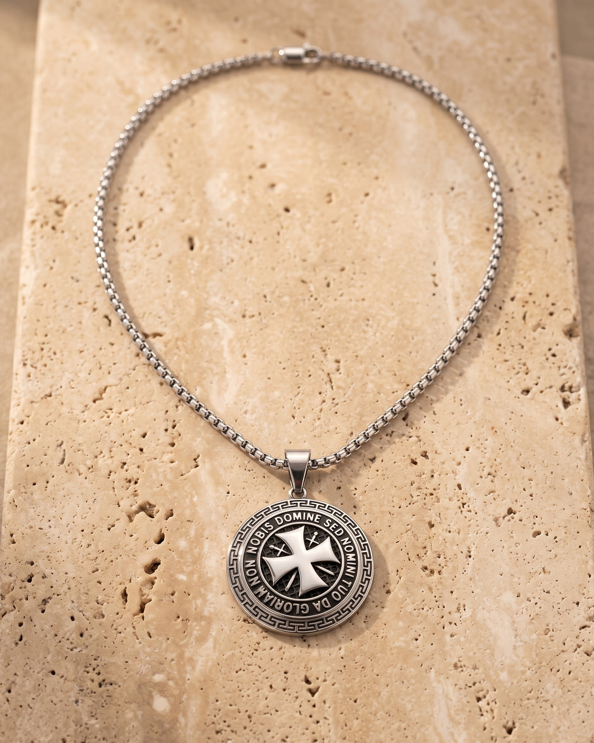 The whole silver-tone Atlas Knights Templar cross medallion necklace lying on warm travertine stone