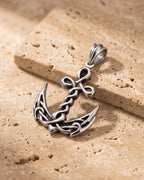 The whole silver-tone Atlas knotwork anchor pendant lying on warm travertine stone