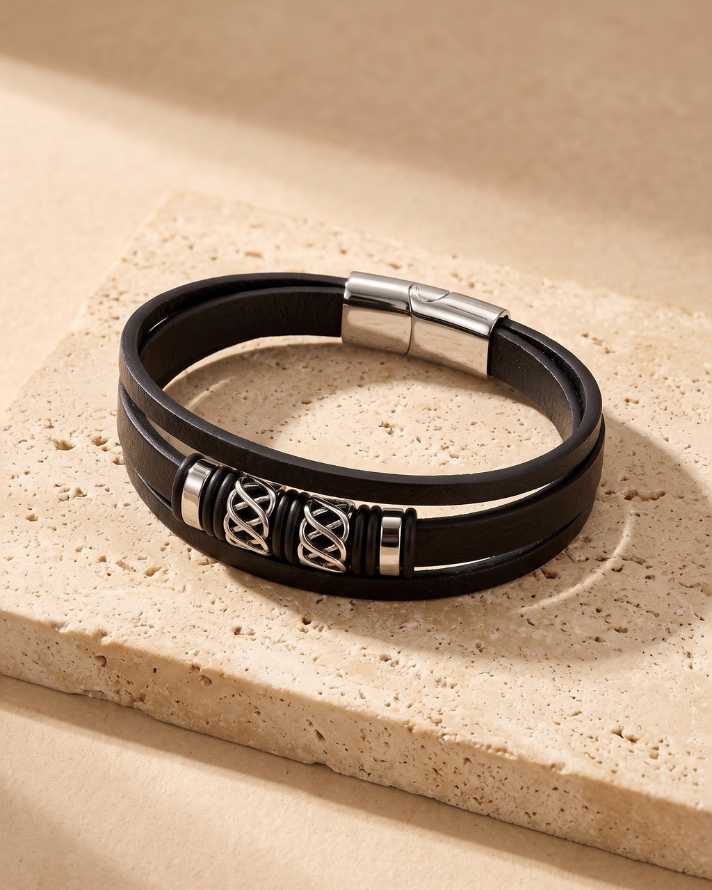 The whole silver Atlas knotwork multi-strand leather bracelet lying on warm travertine stone
