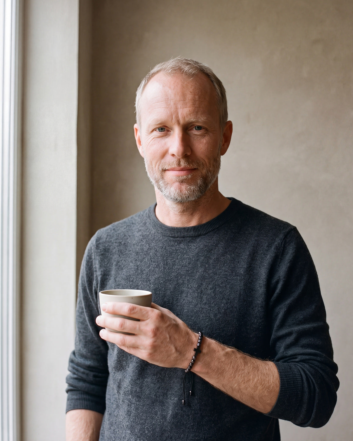 Man in a charcoal sweater holding a coffee cup, wearing the black Atlas knurled cross bead bracelet