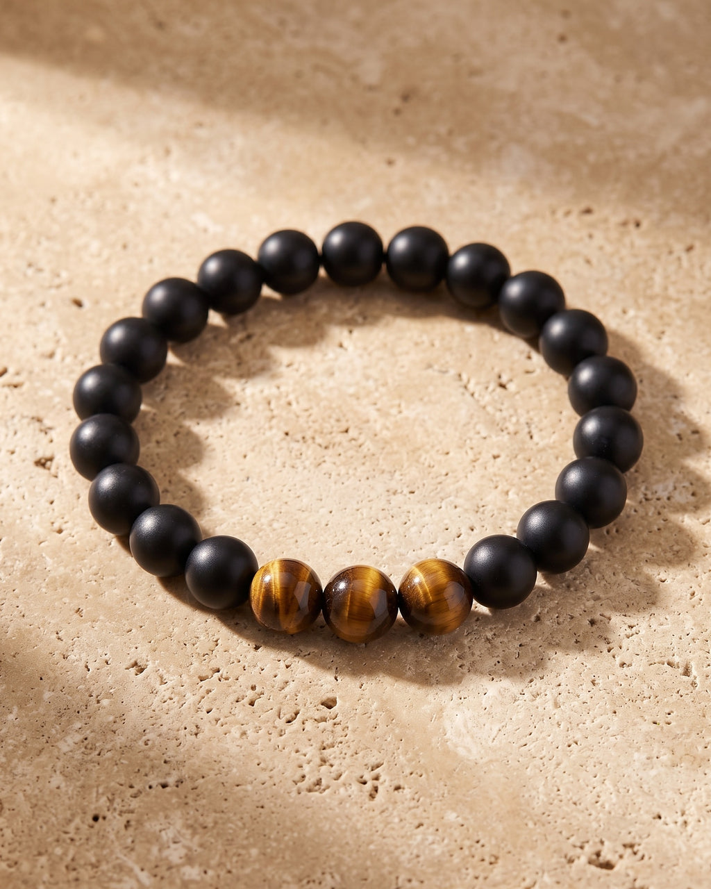 The whole Black & Tiger Eye Atlas Lava and Tiger Eye Stone Bead Bracelet lying on warm travertine stone