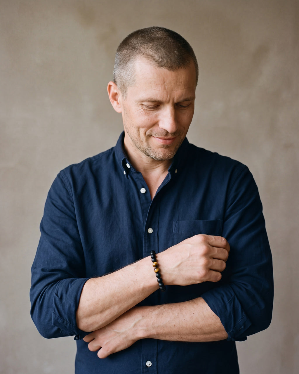 Man in a dark navy cotton oxford shirt by a window wearing the Black & Tiger Eye Atlas Lava and Tiger Eye Stone Bead Bracelet