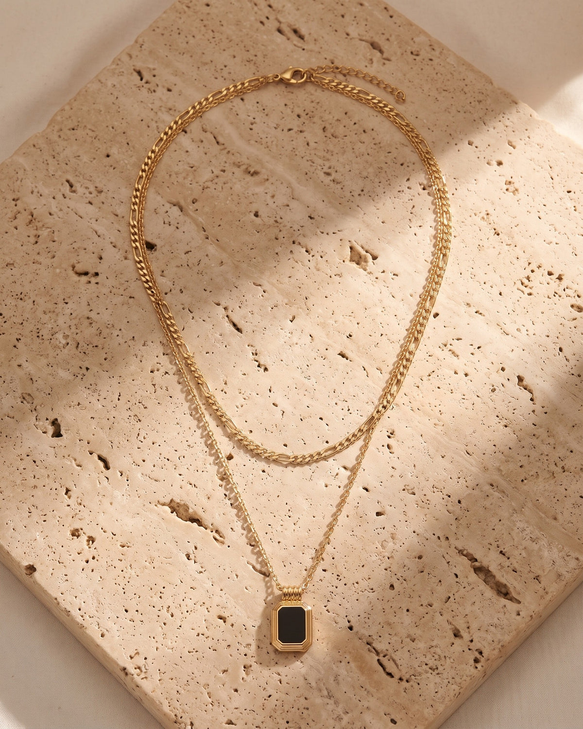 The black Atlas Layered Figaro Chain Necklace laid on warm travertine stone [c:black]
