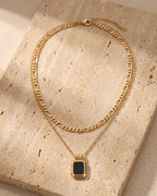 The whole black Atlas Layered Figaro Chain Necklace with Black Stone lying on warm travertine stone