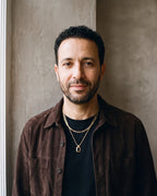 Man in a dark brown suede overshirt open over a black t-shirt by a window wearing the black Atlas Layered Figaro Chain Necklace with Black Stone