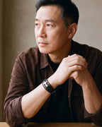 Man in a brown suede overshirt seated at a table, wearing the silver Atlas layered leather cross bracelet