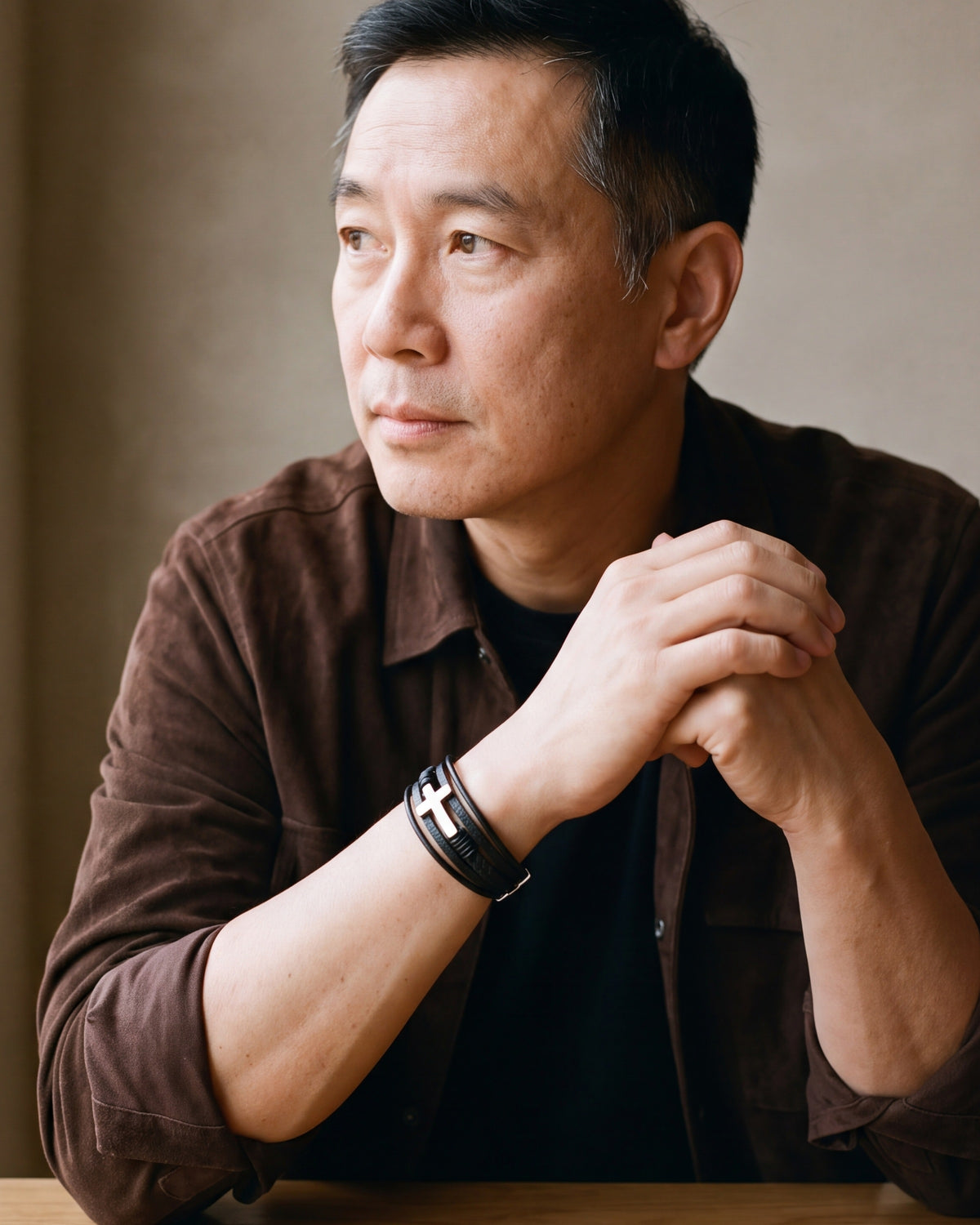 Man in a brown suede overshirt seated at a table, wearing the silver Atlas layered leather cross bracelet