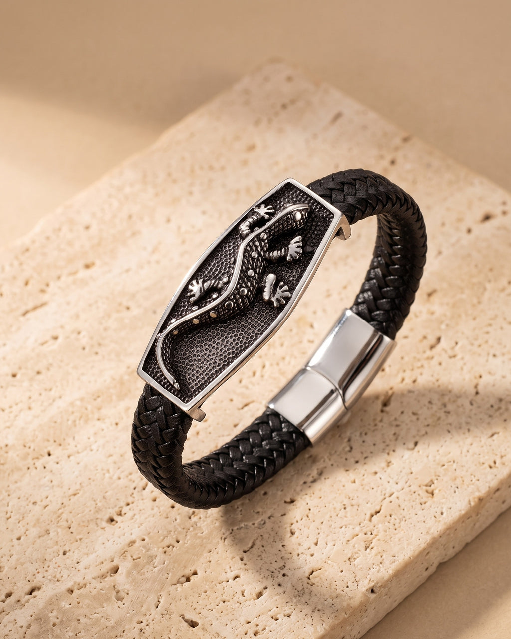 The Atlas lizard plaque braided leather bracelet closed, lying on warm stone