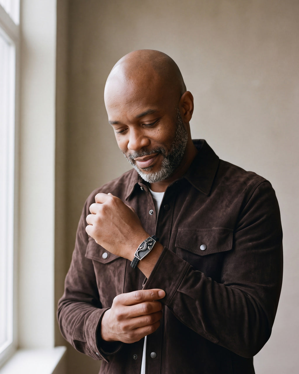 Man in a brown suede overshirt adjusting his cuff, wearing the Atlas lizard plaque braided leather bracelet