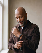 Man in a brown suede overshirt adjusting his cuff, wearing the Atlas lizard plaque braided leather bracelet