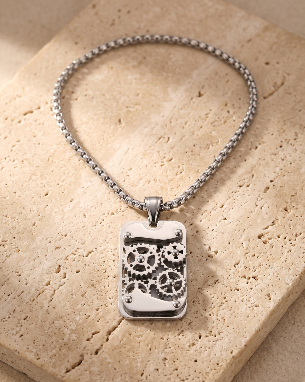 The whole silver-tone Atlas mechanical gear dog tag necklace laid on warm stone