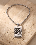 The whole silver-tone Atlas mechanical gear dog tag necklace laid on warm stone