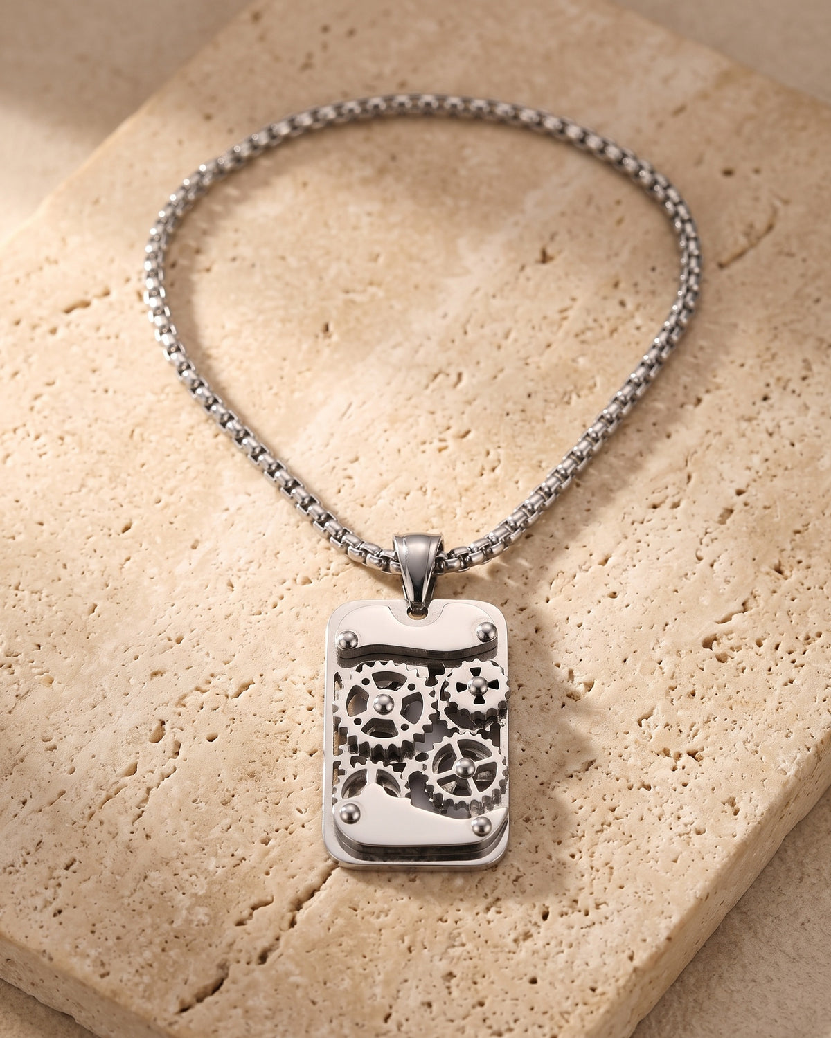 The whole silver-tone Atlas mechanical gear dog tag necklace laid on warm stone