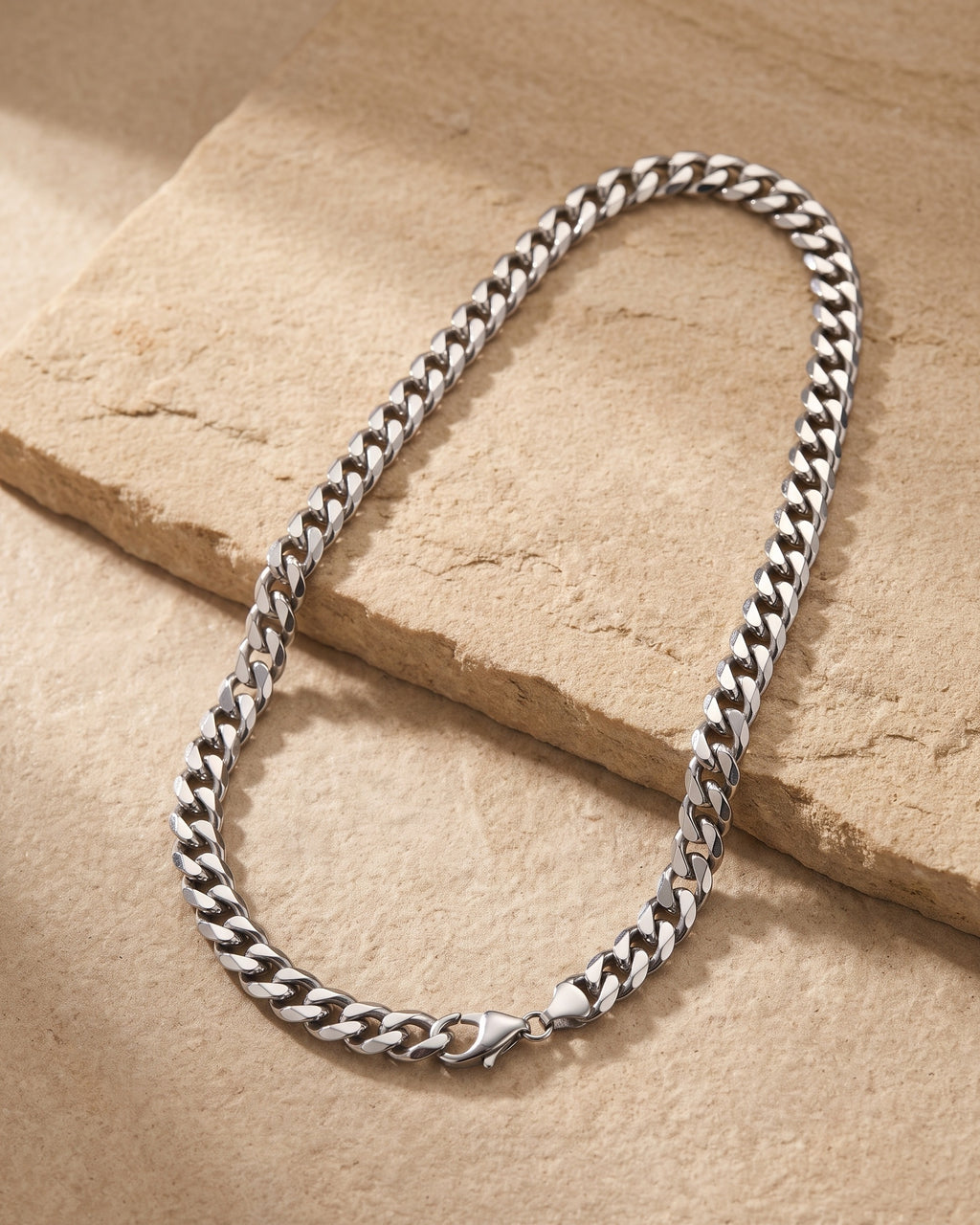 The whole silver Atlas Miami Cuban chain laid on warm stone, lobster clasp closed