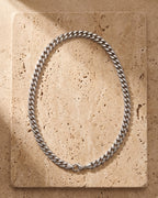The silver Atlas Miami Cuban Link Chain laid on warm travertine stone