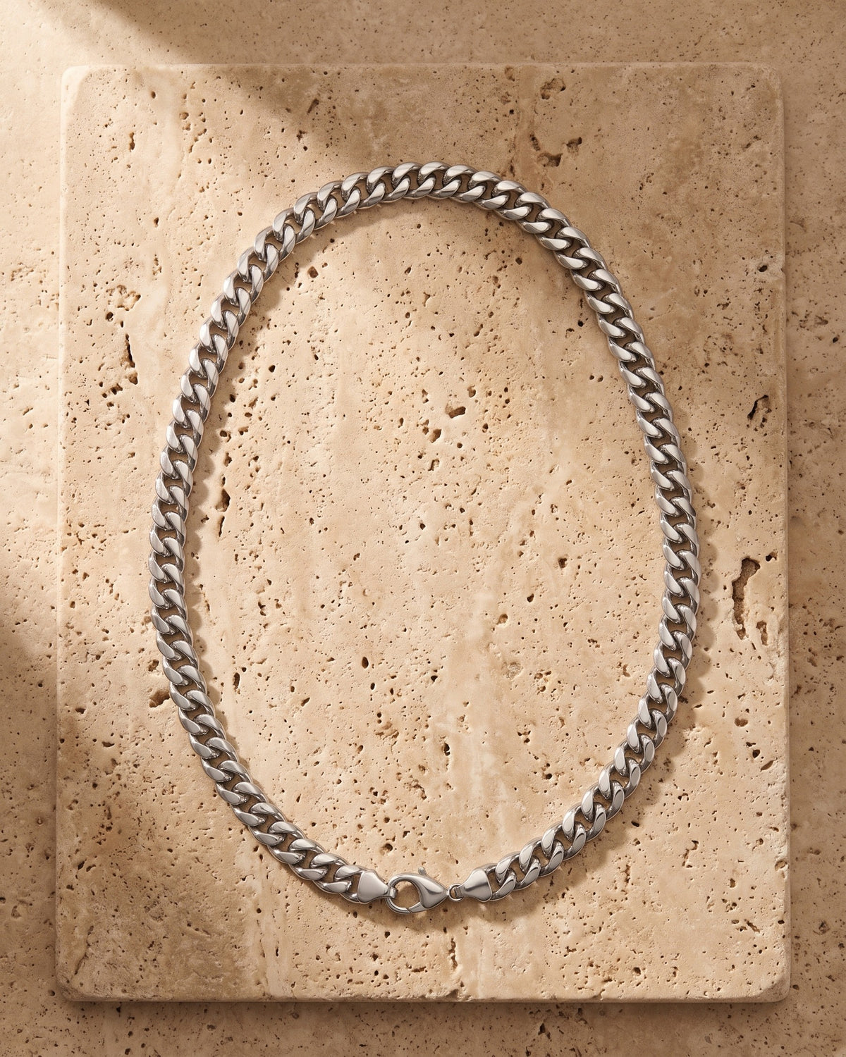 The silver Atlas Miami Cuban Link Chain laid on warm travertine stone
