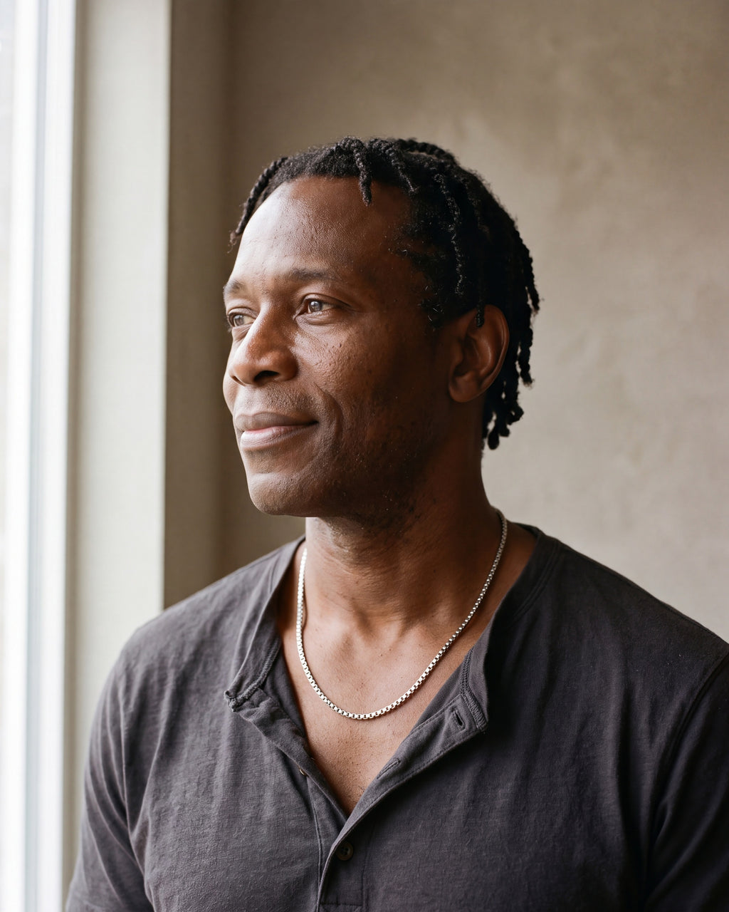 Man in a charcoal cotton henley t-shirt by a window wearing the silver Atlas minimalist box chain