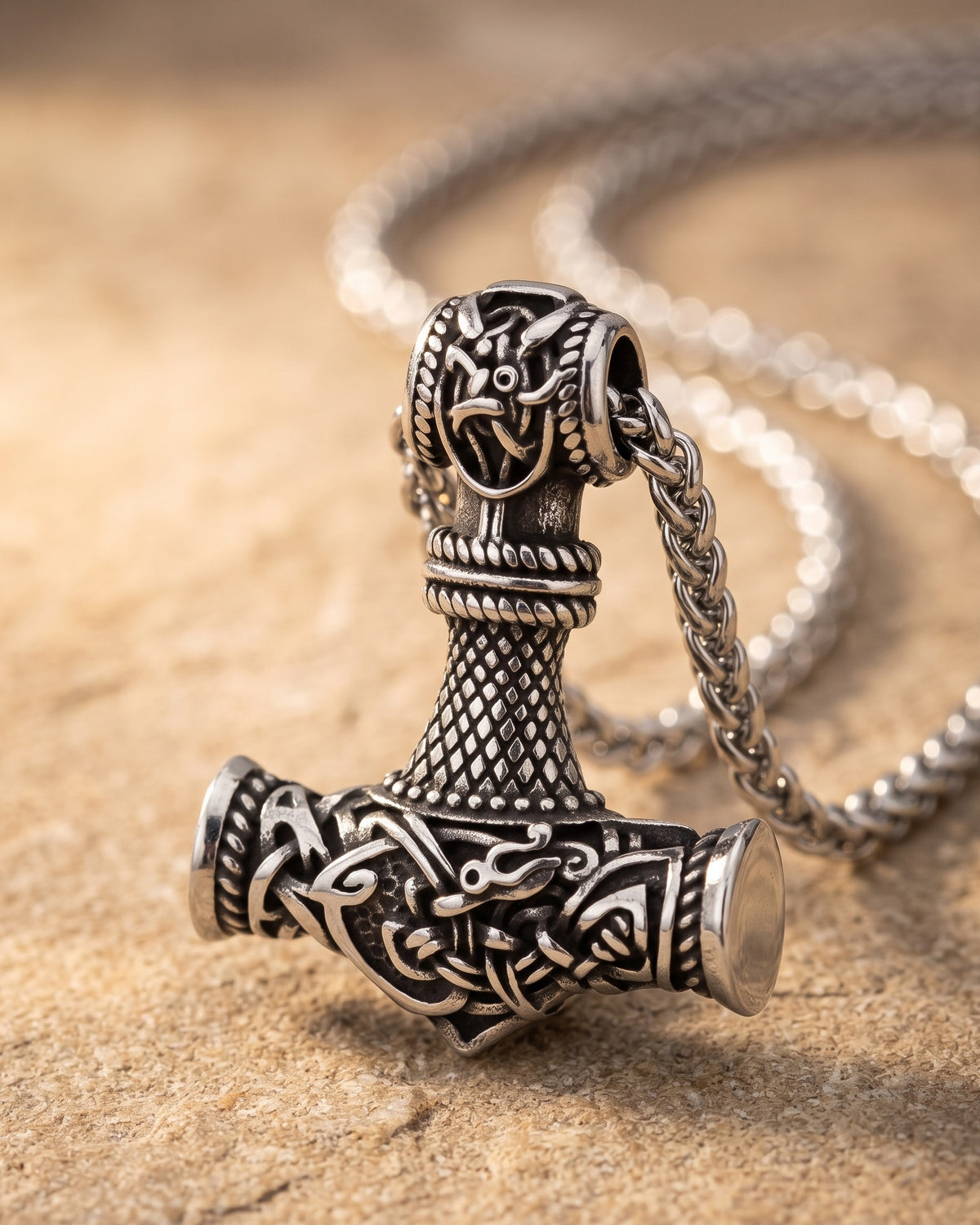 Close-up of the silver-tone Atlas mjolnir hammer pendant necklace resting on warm stone