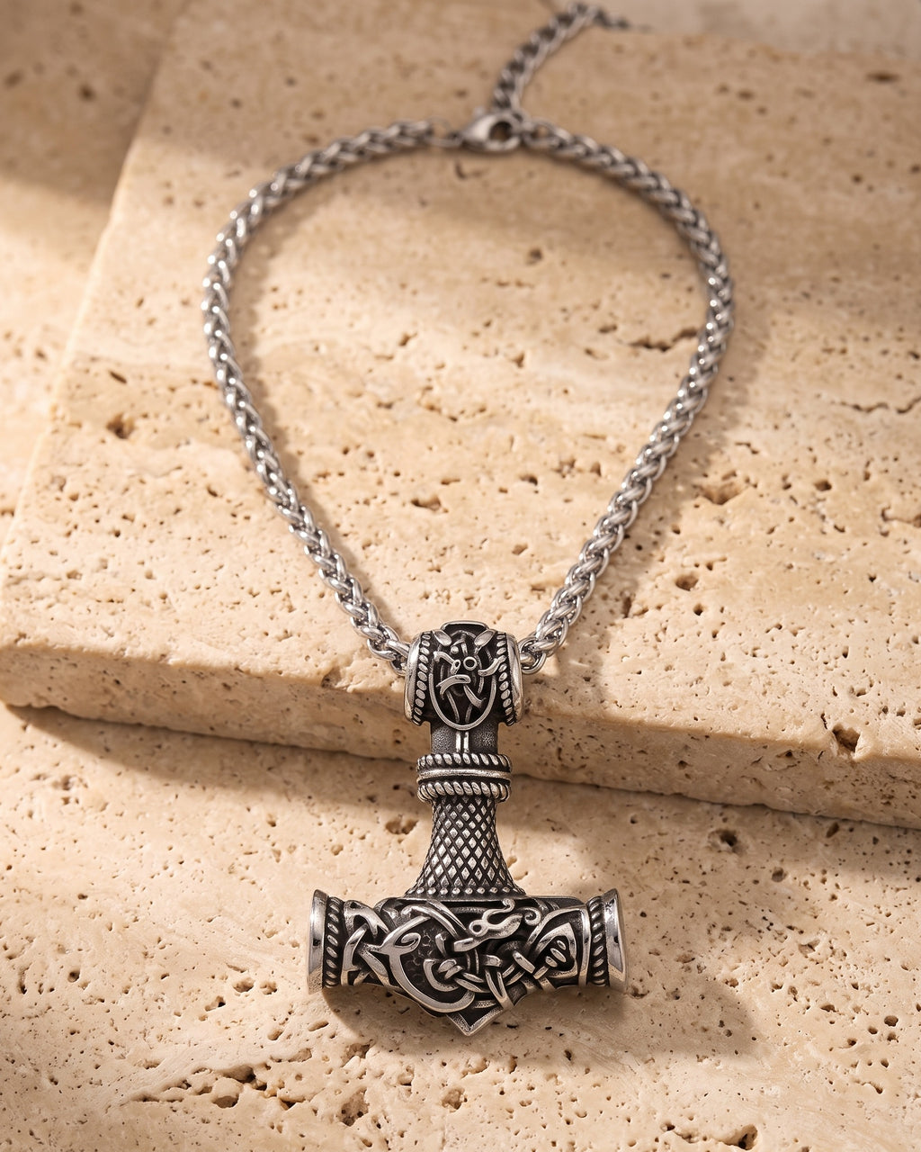 The whole silver-tone Atlas mjolnir hammer pendant necklace lying on warm travertine stone