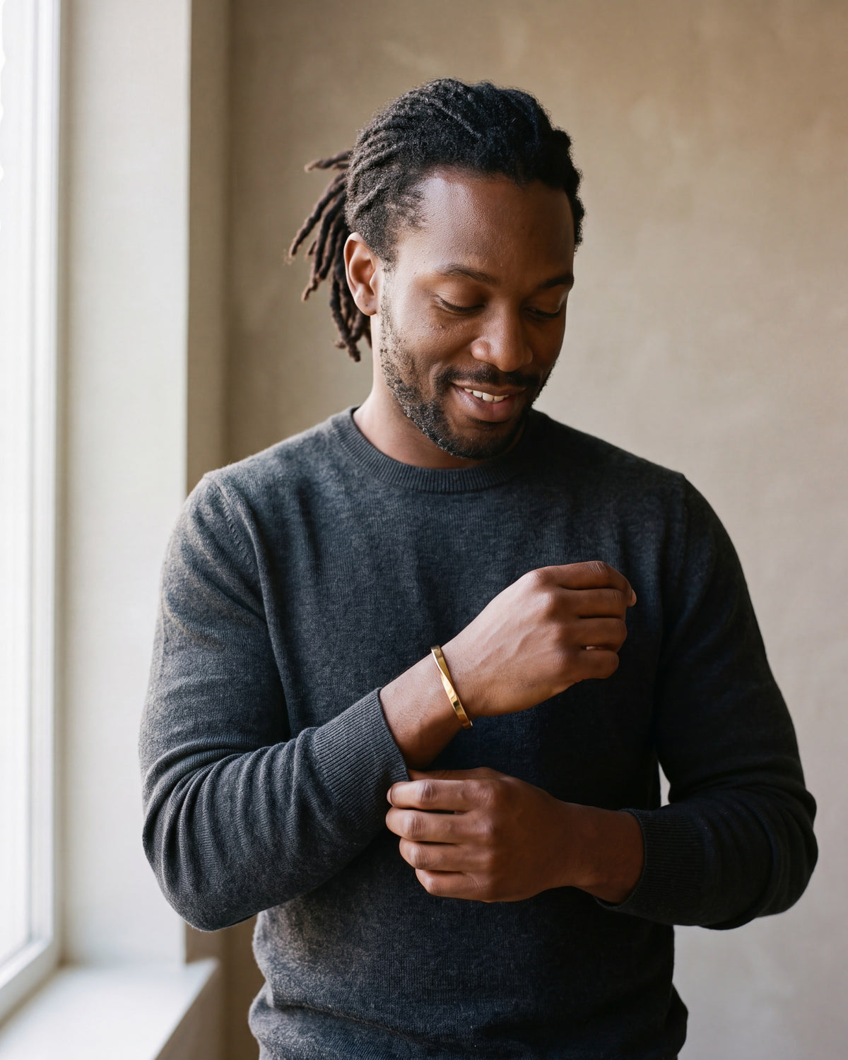 Second man in a charcoal fine-gauge knit crew-neck sweater wearing the gold-tone Atlas mobius twist cuff bracelet