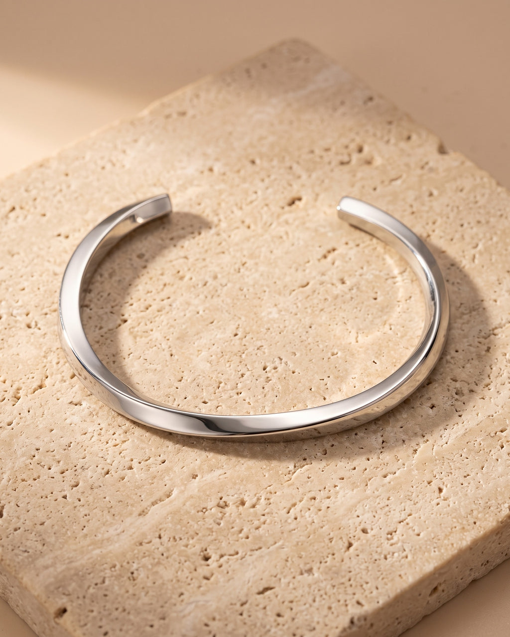 The whole silver-tone Atlas mobius twist cuff bracelet lying on warm travertine stone