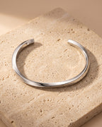 The whole silver-tone Atlas mobius twist cuff bracelet lying on warm travertine stone