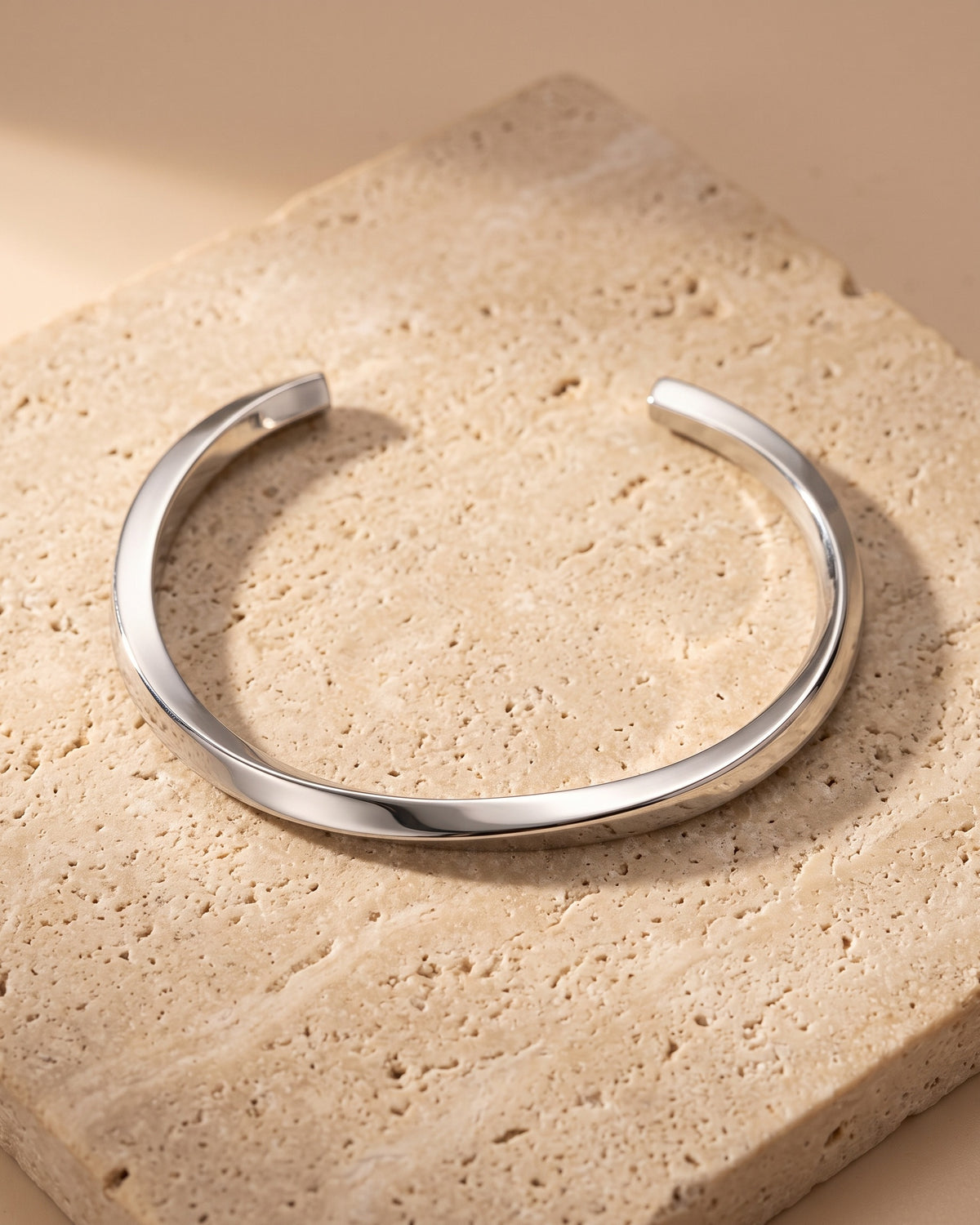 The whole silver-tone Atlas mobius twist cuff bracelet lying on warm travertine stone