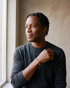 Man in a charcoal fine-gauge knit crew-neck sweater by a window wearing the silver-tone Atlas mobius twist cuff bracelet