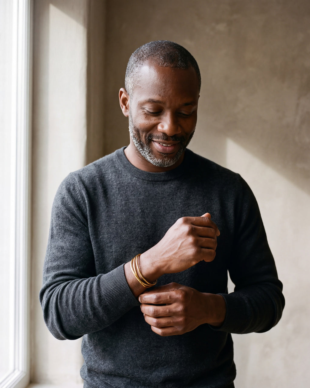 Man in a charcoal sweater adjusting his sleeve wearing the gold-tone Atlas multi-line open cuff bracelet