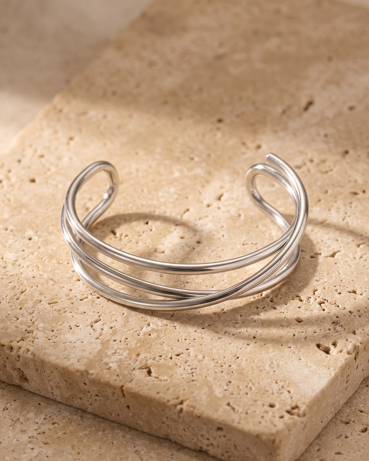 The whole silver-tone Atlas multi-line open cuff bracelet laid on warm stone