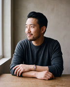 Man in a charcoal sweater seated at a wooden table wearing the silver-tone Atlas multi-line open cuff bracelet