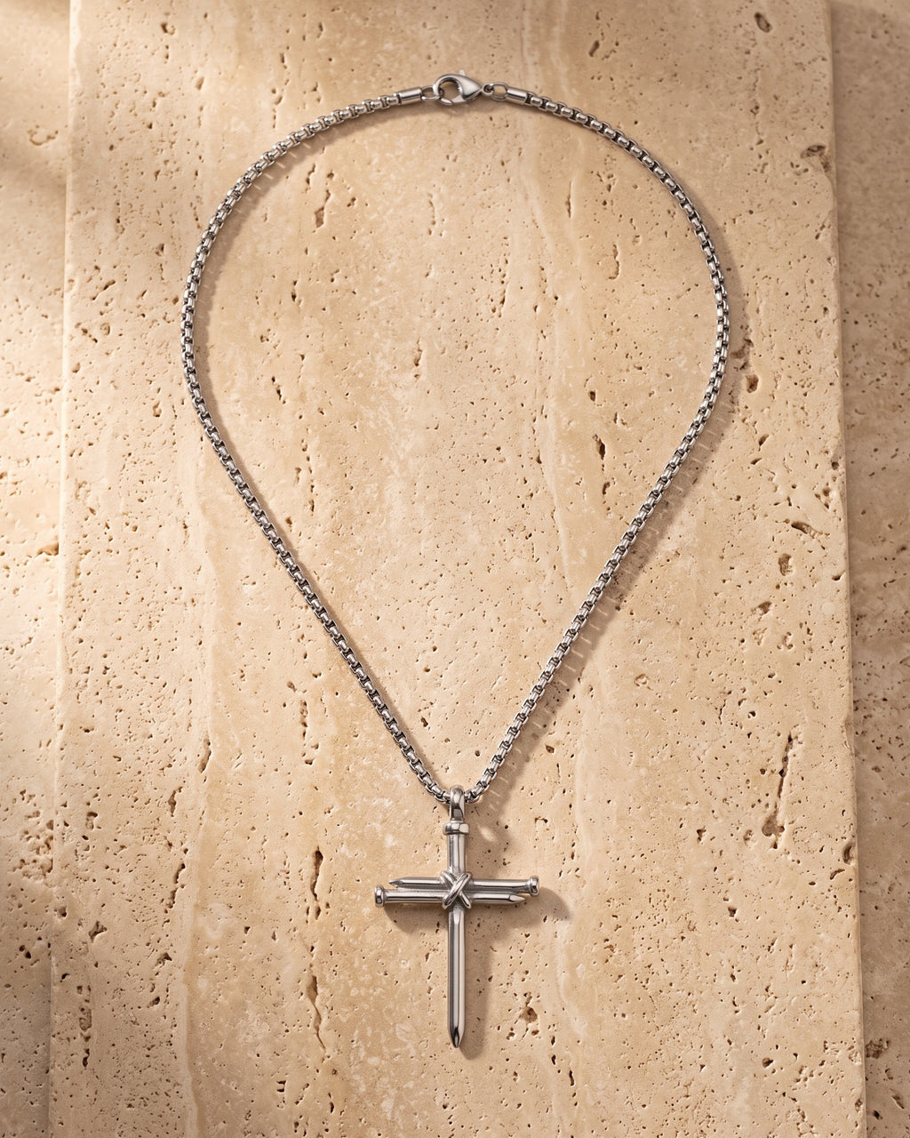 Atlas nail cross pendant and chain laid whole on warm stone