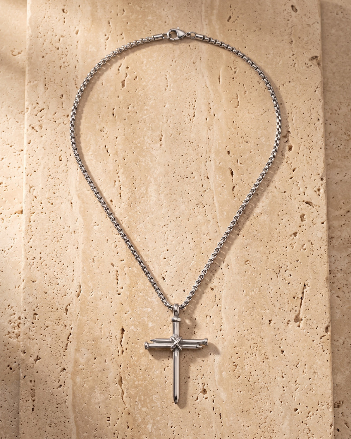 Atlas nail cross pendant and chain laid whole on warm stone