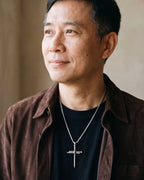 Man in a brown suede overshirt looking toward the window, wearing the Atlas nail cross pendant