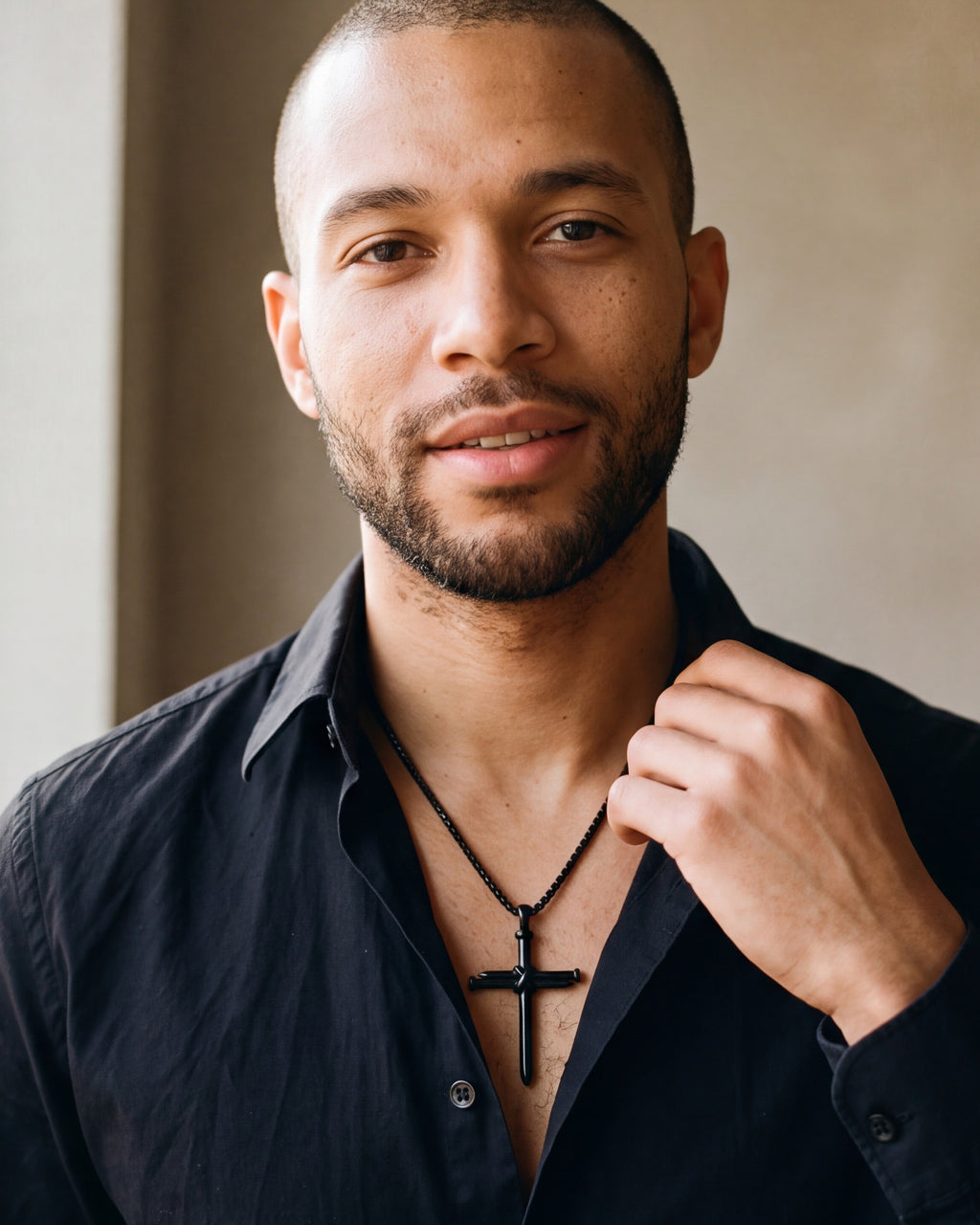 Man in a black shirt with his hand at the collar, wearing the black Atlas nail cross pendant