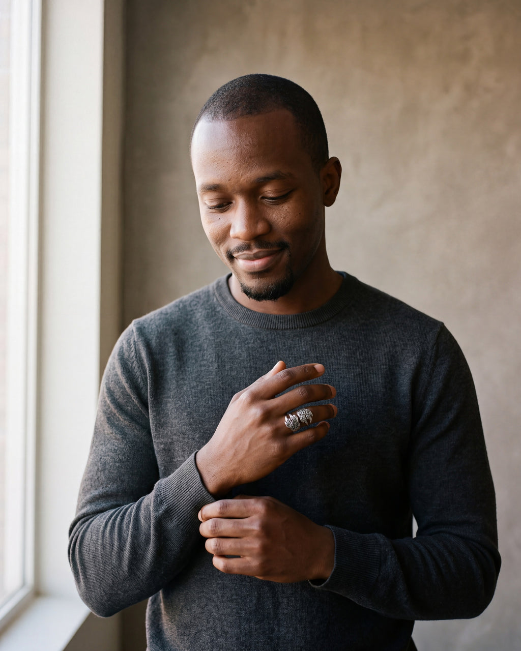 Man in a charcoal knit sweater by a window wearing the Atlas Norse claw adjustable ring in silver-tone steel