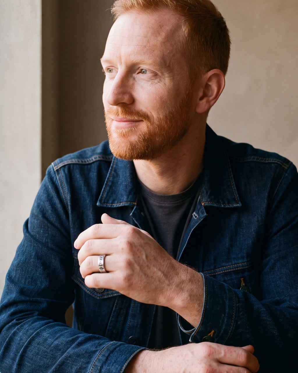 Man in a denim jacket seated at a table, wearing the silver Atlas Norse rune band ring