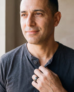 Man in a charcoal henley with his hand at his collar, wearing the black Atlas Norse rune band ring