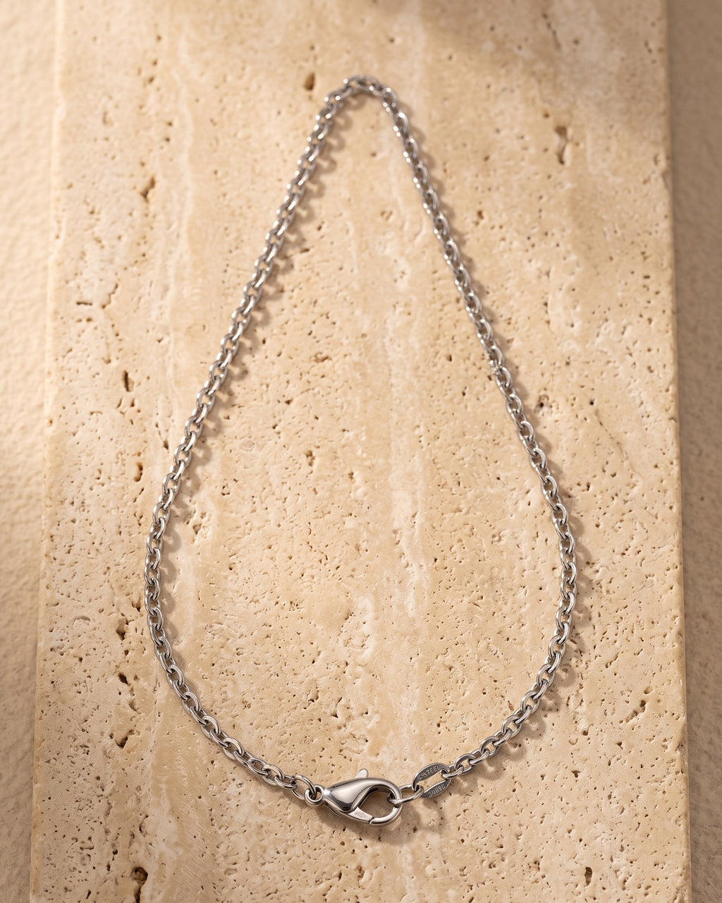 The whole silver-tone Atlas O-link chain laid on warm stone