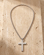 The whole silver-tone Atlas Our Father engraved cross pendant necklace laid on warm stone