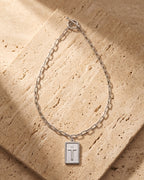 The silver Atlas Paperclip Chain Cross Necklace laid on warm travertine stone