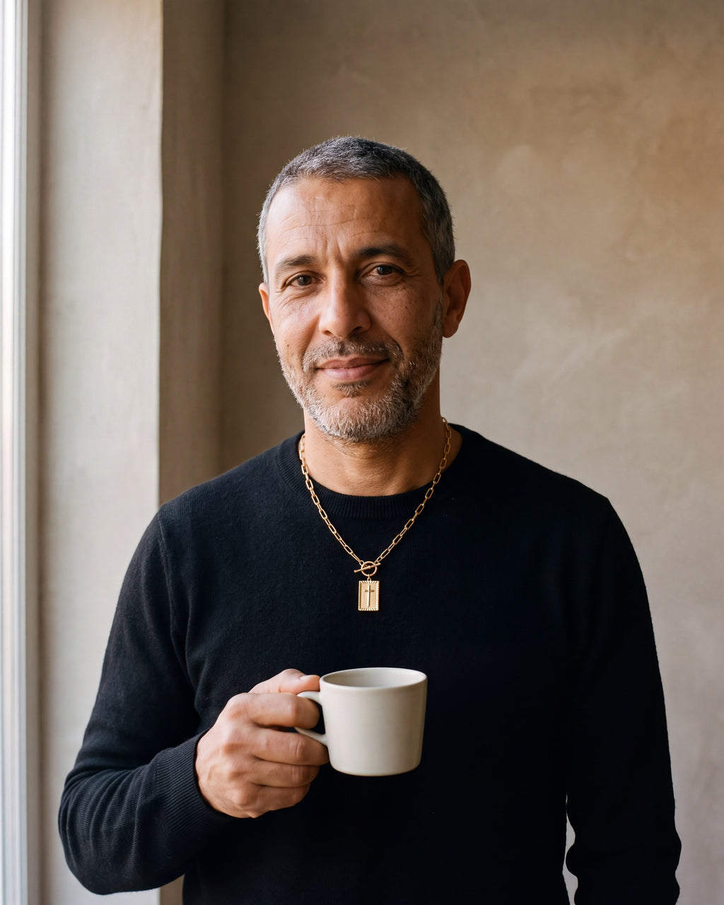 Man in a black merino sweater wearing the Atlas paperclip chain cross tag necklace in gold-tone steel