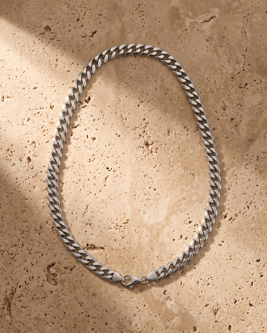 The silver Atlas Polished Cuban Chain in Titanium Steel laid on warm travertine stone