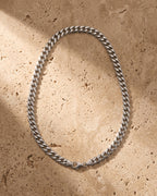 The silver Atlas Polished Cuban Chain in Titanium Steel laid on warm travertine stone