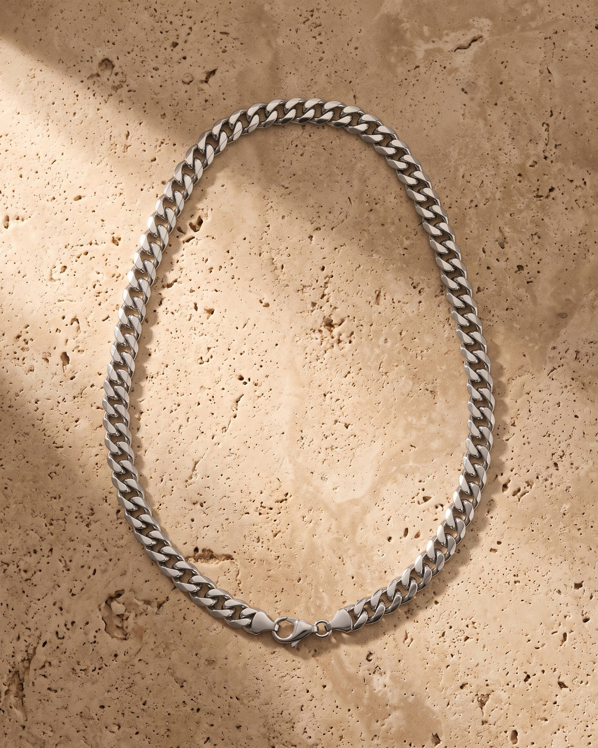 The silver Atlas Polished Cuban Chain in Titanium Steel laid on warm travertine stone