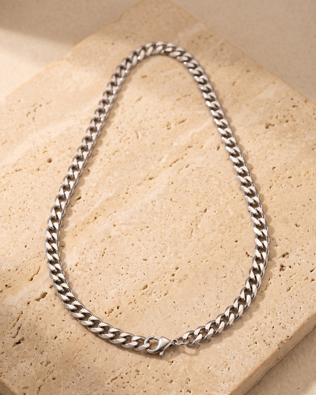 The whole silver Atlas polished Cuban chain laid on warm stone, lobster clasp closed