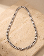 The whole silver Atlas polished Cuban chain laid on warm stone, lobster clasp closed