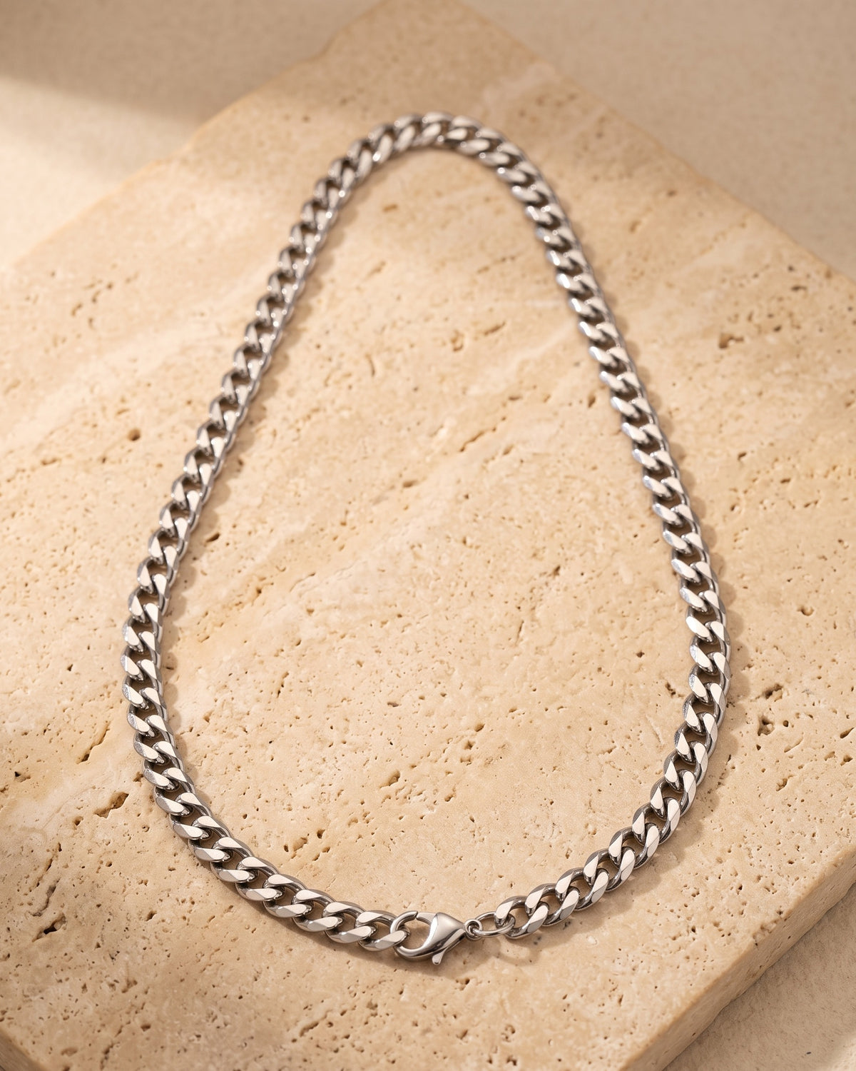 The whole silver Atlas polished Cuban chain laid on warm stone, lobster clasp closed